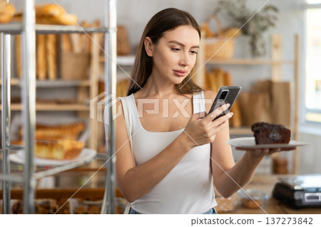 Female customer takes a photo of a sweet pie using a smartphone in the interior of private bakery 137273842