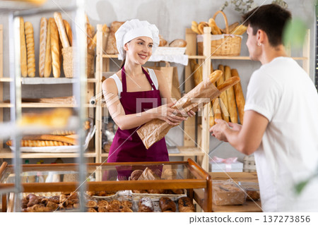 Young woman seller gives baguette to man buyer Young woman seller gives baguette to man buyer 137273856