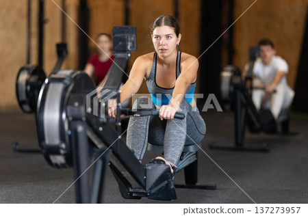 Focused girl works out with rowing machine during class at fitness club 137273957
