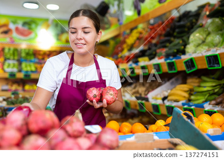 Girl seller working in supermarket and lays out pomegranate on counter Girl seller working in supermarket and lays out pomegranate on counter 137274151