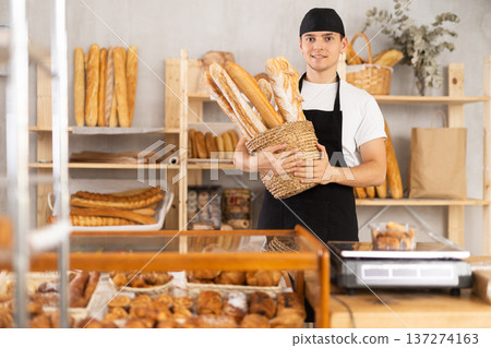 Young smiling man baker offers to buy fresh delicious baguettes Young smiling man baker offers to buy fresh delicious baguettes 137274163