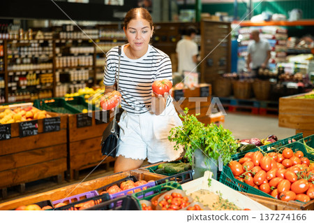 Interested young girl choosing ripe tomatoes on display in store 137274166