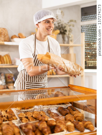 Friendly guy offers to buy hot baguettes to customer in bakery interior Friendly guy offers to buy hot baguettes to customer in bakery interior 137274173
