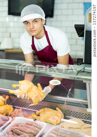 In butcher shop, young male salesperson in gloves shows damp dressed chicken In butcher shop, young male salesperson in gloves shows damp dressed chicken 137274197