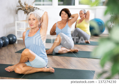 Old woman practicing cow face pose of yoga in training room during fitness classes Old woman practicing cow face pose of yoga in training room during fitness classes 137274230