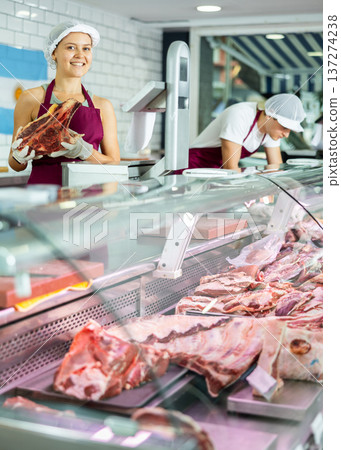 Positive young saleswoman demonstrating piece of meat in butcher shop 137274238