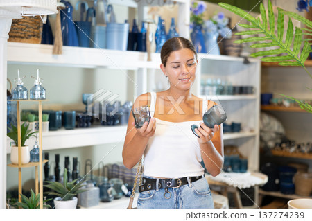 Girl examining blue glass goblet and tumbler in home decor store Girl examining blue glass goblet and tumbler in home decor store 137274239