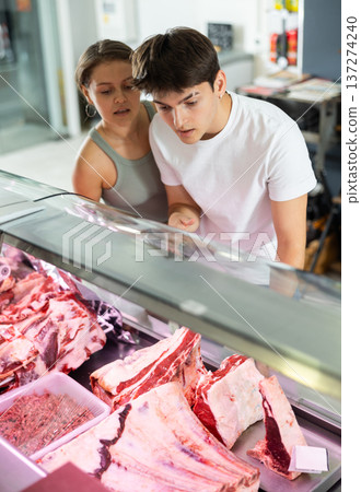 Spouse near butcher shop window inspects goods and choose piece of beef for cooking rib eye steak Spouse near butcher shop window inspects goods and choose piece of beef for cooking rib eye steak 137274240