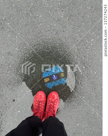 下雨天，一雙穿著紅色運動鞋的腳站在水坑裡。 137274243