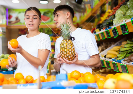 Male and female customers in casual clothes buying pineapples and oranges in grocery store Male and female customers in casual clothes buying pineapples and oranges in grocery store 137274384