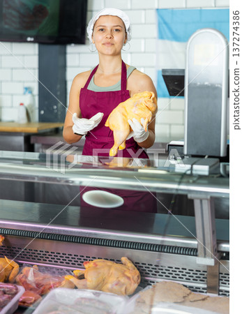 In butcher shop, young female salesperson in gloves shows damp dressed chicken In butcher shop, young female salesperson in gloves shows damp dressed chicken 137274386
