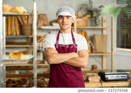Young male seller in sales area of bakery stands near counter and waits for visitors. 137274396