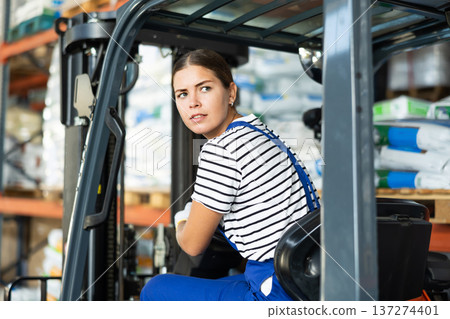 Girl works on fork lift loader in construction rack area warehouse store repair materials. 137274401