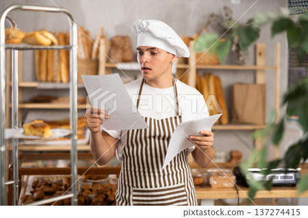 Focused young bakery worker checking order form 137274415