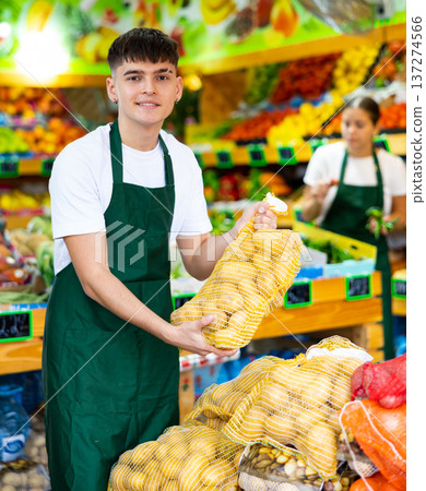 Young male seller laying out and offering bag of potatoes in grocery store 137274566