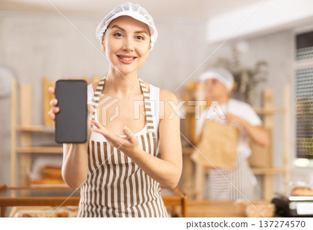 Smiling female bakery owner demonstrating mobile app for online orders Smiling female bakery owner demonstrating mobile app for online orders 137274570