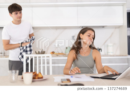 Young girl sitting at the table while her boyfriend is quarreling with her standing behind 137274689