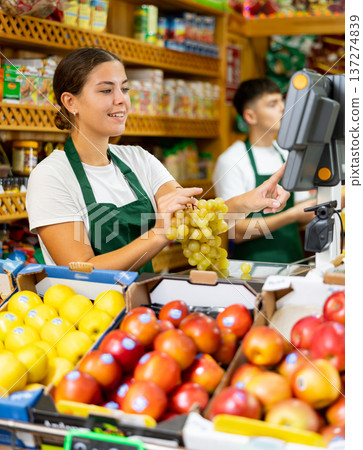Smiling european female seller weighing grape in supermarket Smiling european female seller weighing grape in supermarket 137274839