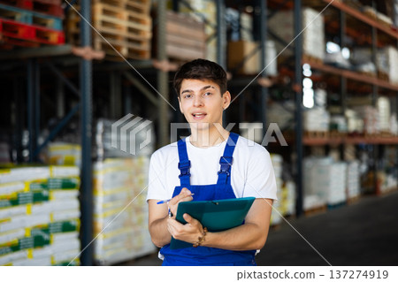 In warehouse of store, guy checks quantity of goods and receipt documents for products 137274919