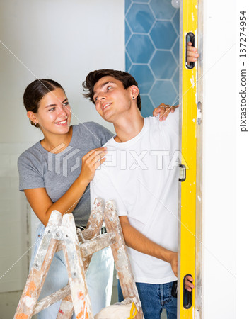 Young couple uses a spirit level on the wall Young couple uses a spirit level on the wall 137274954
