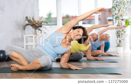 Old woman practicing lotus pose of yoga with side bend in training room 137275000