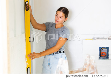 Portrait of a young woman using a spirit level on the bathroom wall 137275062