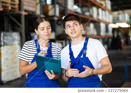 Girl check papers invoices together with guy employee and revise availability of goods in stock Girl check papers invoices together with guy employee and revise availability of goods in stock 137275064