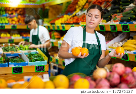 Young female seller lay out ripe oranges on counter in supermarket 137275127