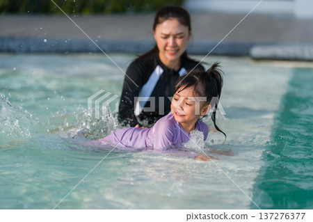 mother with preschool child girl kicking water splashing by her legs while practicing swimming in edge of pool mother with preschool child girl kicking water splashing by her legs while practicing swimming in edge of pool 137276377