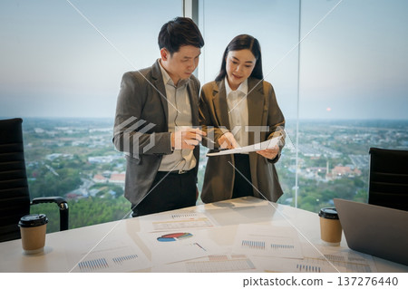 Two coworkers discussing work and pointing at documents of paperwork in meeting room. business people in office 137276440