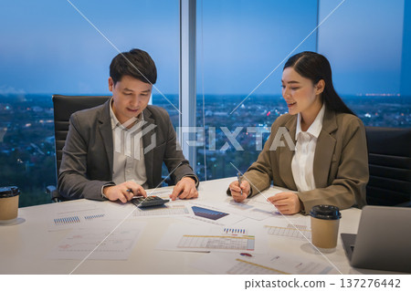 two business colleagues meeting and discussing financial reports and using calculator to data analysis in office at night two business colleagues meeting and discussing financial reports and using calculator to data analysis in office at night 137276442
