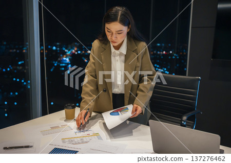 businesswoman thinking and analyzing business reports late at night in office with city lights background 137276462