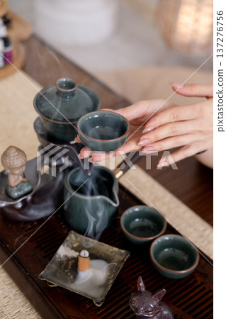 Herbal drink. Chinese tea ceremony. Table with tea-board woman hand holding water vapor incense cup figurine. Herbal drink. Chinese tea ceremony. Table with tea-board woman hand holding water vapor incense cup figurine. 137276756