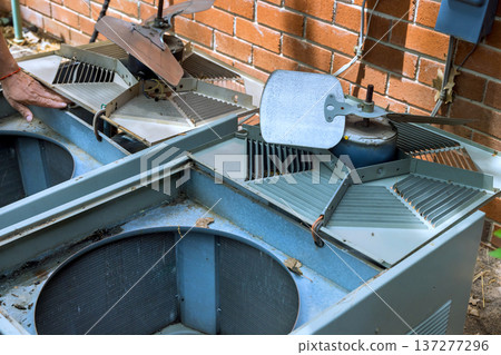 Technician works on fixing two air conditioning units located outside brick building in residential neighborhood. 137277296