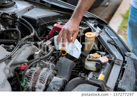 Worker inspects engine components wipes fluid caps while performing vehicle maintenance in service garage Worker inspects engine components wipes fluid caps while performing vehicle maintenance in service garage 137277297