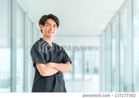 A young Asian man wearing a scrub and crossing his arms, a doctor, nurse, caregiver, or emergency physician A young Asian man wearing a scrub and crossing his arms, a doctor, nurse, caregiver, or emergency physician 137277302