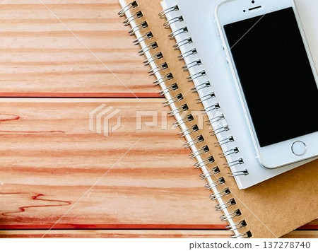 A smartphone and two notebooks placed on a wooden table 137278740