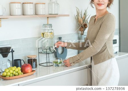 一位女士正在廚房檯面上從飲水機倒排毒水。 一位女士正在廚房檯面上從飲水機倒排毒水。 137278936