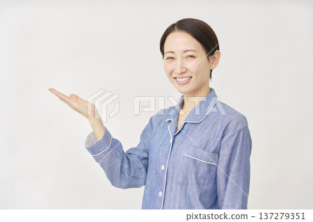 A woman in pajamas pointing to the left with her palm on a white background 137279351