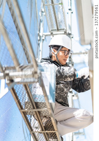 一名戴著安全帽的男工人在高空危險地塗三層油漆。 137279561