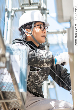A male worker wearing a helmet paints three coats at a dangerous height 137279562