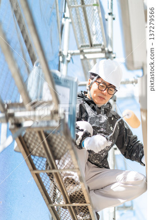 A male worker wearing a helmet paints three coats at a dangerous height A male worker wearing a helmet paints three coats at a dangerous height 137279566