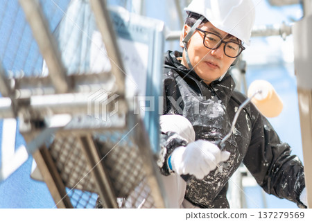 一名戴著安全帽的男工人在高空危險地塗三層油漆。 一名戴著安全帽的男工人在高空危險地塗三層油漆。 137279569