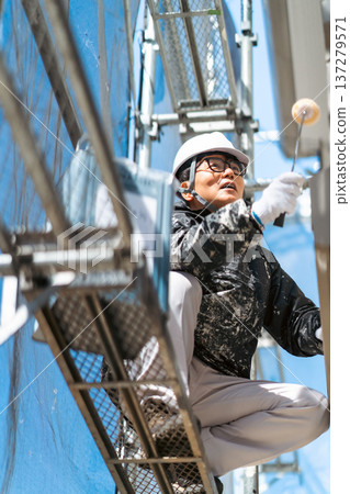 一名戴著安全帽的男工人在高空危險地塗三層油漆。 一名戴著安全帽的男工人在高空危險地塗三層油漆。 137279571