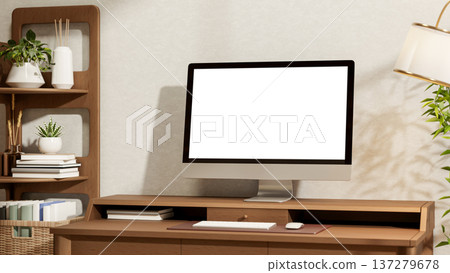 Blank screen computer on wooden table between display bookshelf and lamp with houseplant in sunlight 137279678