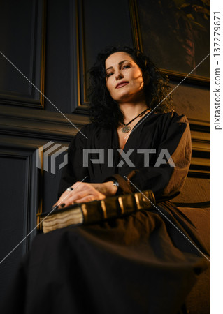 Woman holding a book in a dark room with elegant wall details and soft lighting Woman holding a book in a dark room with elegant wall details and soft lighting 137279871