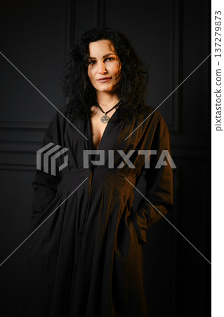 Woman with dark hair stands indoors wearing a black outfit Woman with dark hair stands indoors wearing a black outfit 137279873