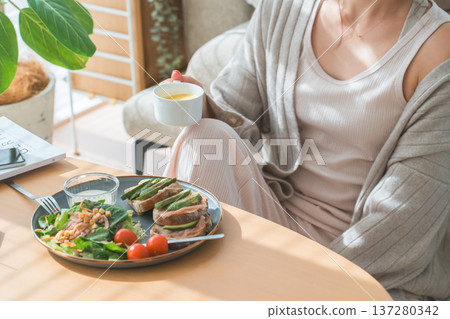 一位時尚的年輕亞裔女性正在客廳餐桌旁用餐。 137280342
