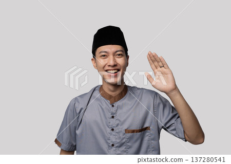 Smiling man waving confidently. Eager Asian man in casual attire greeting enthusiastically 137280541