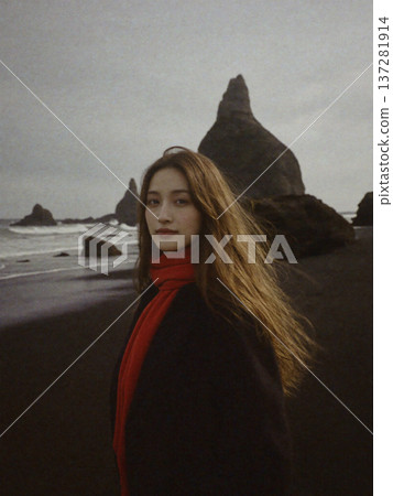 A Japanese woman wearing a red scarf standing on the beach under a cloudy sky 137281914